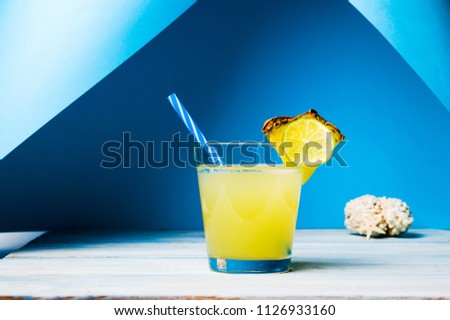 Pineapple juice in a glass with fruit against blue background