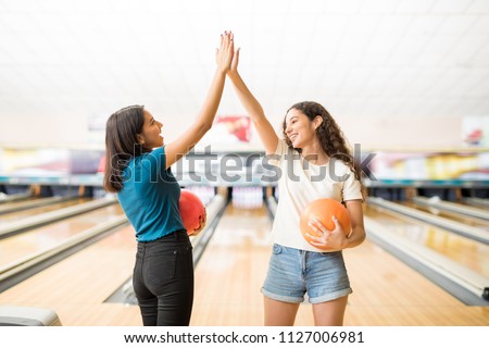 Teenage girls giving high-five before starting bowling game at alley in club