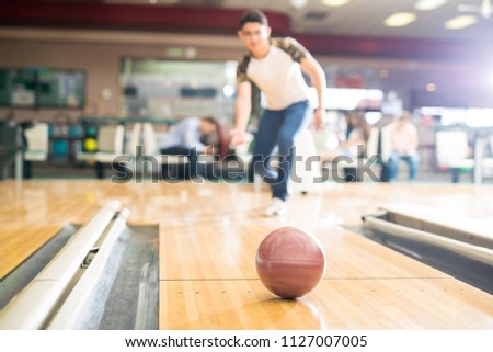 Full length of teenage boy bowling in club with focus on brown ball