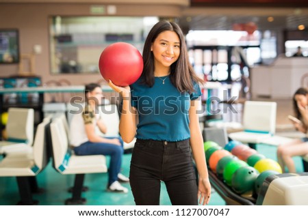 Pretty smiling teenage girl carrying red bowling ball in club