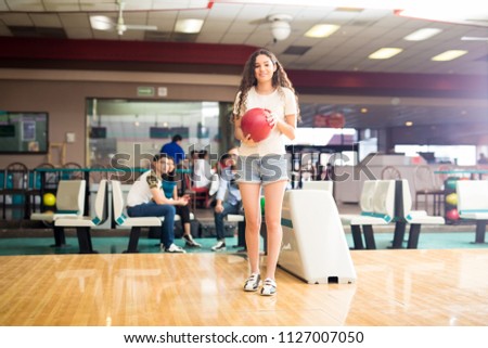 Full length of beautiful teenage bowler playing bowling in alley