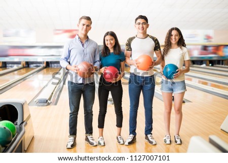 Full length of teenage boys and girls with colorful bowling balls standing in club