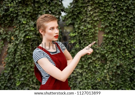   young woman in a red sarafan showing a finger in the place of a free street                             