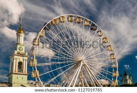 Ferris wheel with bell tower and church on blue cloudy sky background