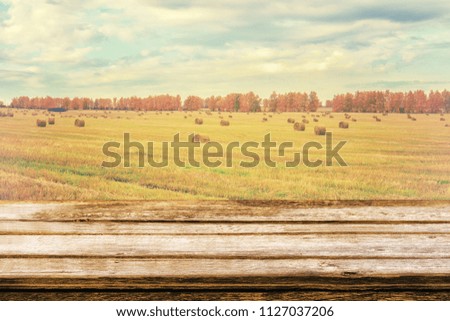 Empty wooden table with autumn landscape of beveled field and straw bales. Can be used for display or montage products