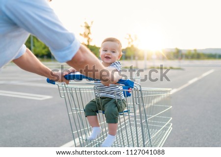 Boy sitting in the shopping cart at supermarket.  Father pushing baby in grocery store. Baby in the shopping cart. Father and son in shopping. Family, childhood, fatherhood and people concept
