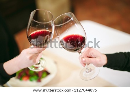 Man and woman drinking red wine. In the picture, close-up hands with glasses. 