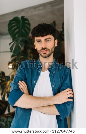 Attractive bearded man with serious face wearing stylish casual shirt posing for pictures in loft cafe. Portrait of successful entrepreneur. Small business owner concept. 