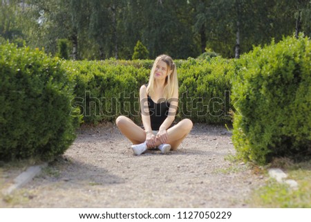Young beautiful woman is warming in the sun sitting on the green grass in the park, on a wonderful summer day.