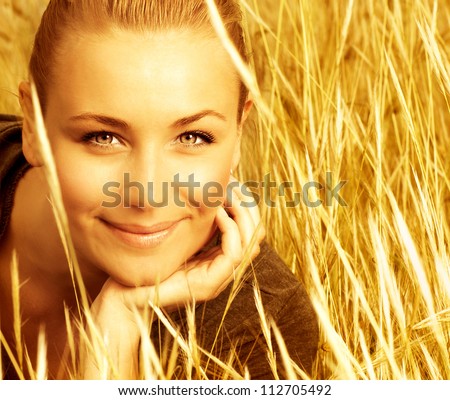 Picture of attractive smiling girl sitting in golden wheat field, closeup portrait of beautiful young blond female on yellow ryes background, enjoying countryside, autumn season of grain harvest