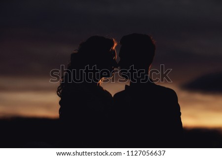 Groom is holding and kissing his bride on the background sunset. Bride and Groom at Sunset.