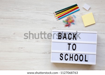 Education concept. Eraser, pencils, stickers, paper clips and 'Back to school' word on a modern board over a white wooden surface. From above, overhead. Copy space.