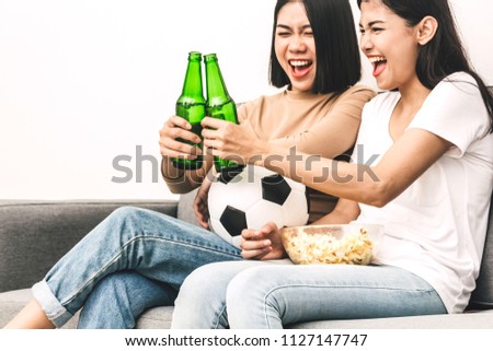 Two woman friends eating popcorn and drinking beer together and watching soccer game on sofa at home.Friendship and party concept