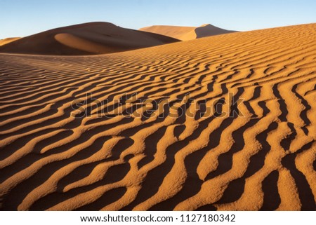Orange, textured, patterned, lined and shadowed sand and sand hills with blue sky in Hiddenvlei Namibia, Africa.