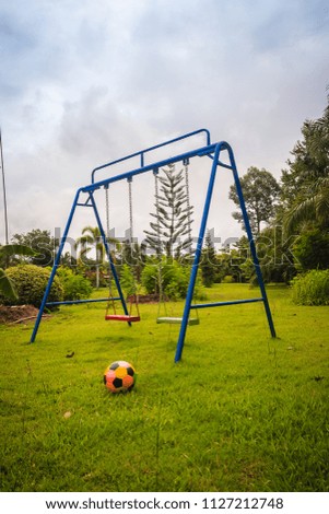 Playground equipment in the backyard for kids with soccer goal net and football on green grass field background.