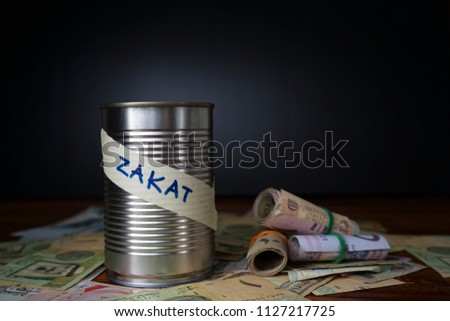 Payment of zakat is a form of charity in Islam. The can with text zakat in blurry black background.