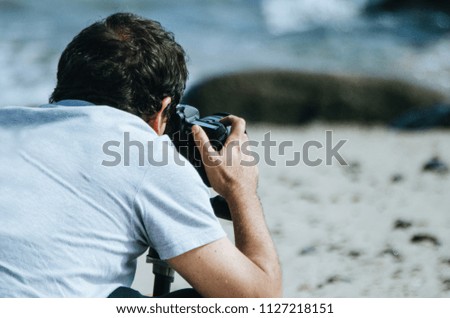 Traveling and photography. Young man with camera taking picture on the sea beach.