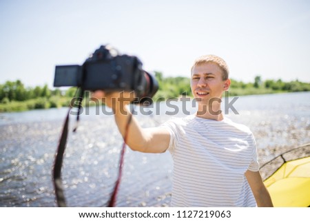 A happy young guy portrait makes a selfie. A cute tourist makes funny photos for a travel blog in nature. on the river bank. the concept of outdoor activities. marketing photographer