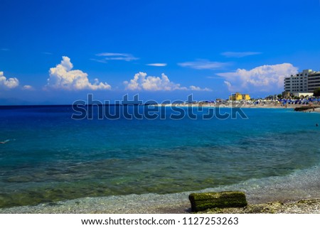 A picturesque summer beach with pebbles in the surf line on a beautiful sea in Rhodes, Greece. travel, recreation. Sea background, space for text, summer rest, summer vacation