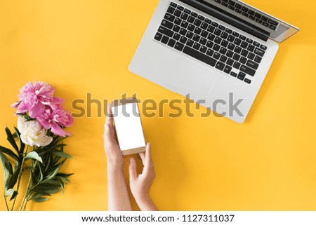 Top view of yellow desk with computer laptop, pink peony flowers, mobile phone, social media. Flat lay.