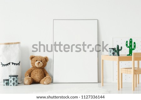 Mockup poster, teddy bear and material basket placed on the floor in white room interior with wooden table and small chair. Paste your photo here Royalty-Free Stock Photo #1127336144