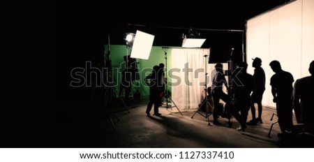 Blurred images of behind the scenes TV commercial movie film or video shooting production which crew team and camera man setting up green screen for chroma key technique in big studio.