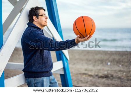 Side view of man holding basketball and looking away while standing on beach
