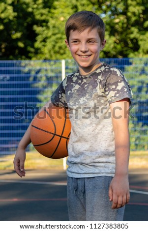 Pre-teen boy holding a basketball on a court in a park