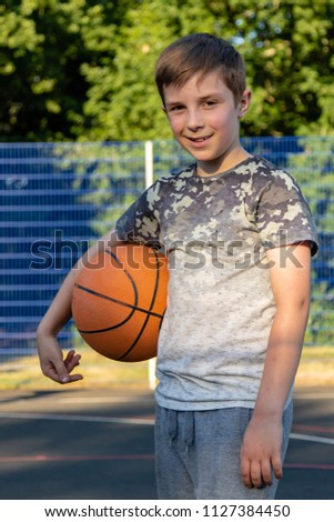 Pre-teen boy holding a basketball on a court in a park