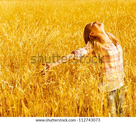Picture of cheerful teenager having fun in countryside, cute happy female standing on wheat field with raised open hands and looking up, blond girl enjoying autumn nature, fall season