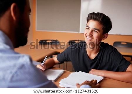 High School Tutor Giving Male Student One To One Tuition At Desk Royalty-Free Stock Photo #1127431520