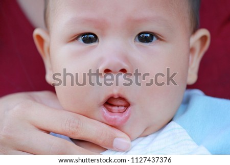 Mother hands open baby mouth to examine first teeth. Infant primary tooth.