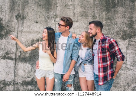 A picture of chinese girl looking to the left. Also she is pointing to that side. Her friends are standing very close to her and looking at the same direction. Standing on grey background.
