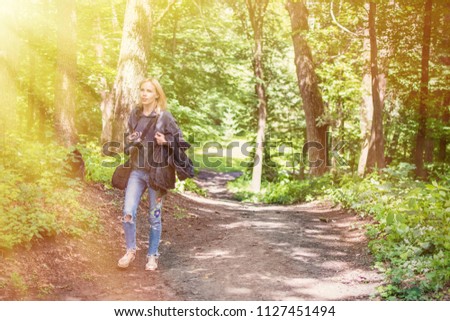 A woman photographer is walking along a forest path with a camera.