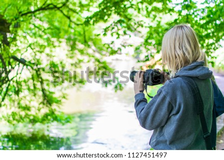 Woman photographer taking photo in a green forest in the summer.