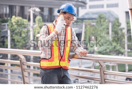 Handsome male engineering worker in hardhat and uniform while talking on the phone in construction site work.