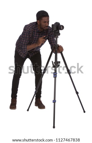 A full-length shot of a young African photographer holding a camera stand and shooting, isolated on a white background.