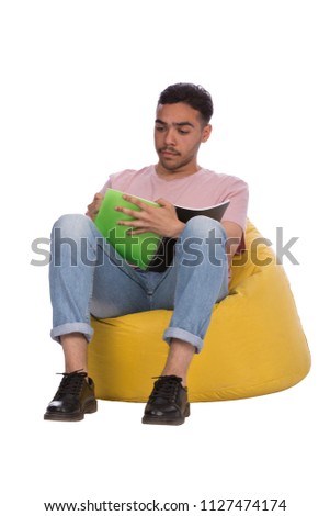 young man studying on a bean bag holding a notebook, isolated on a white background.