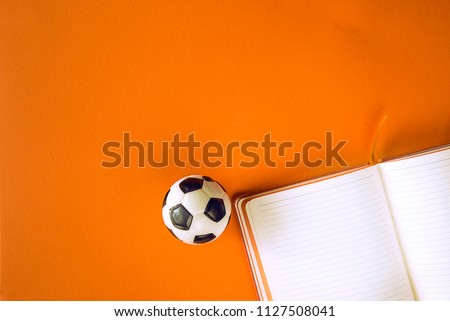 One white and black ball for football and notebook on orange background with copy space