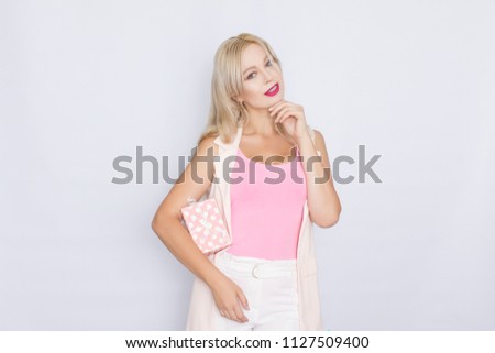 business portrait of a blond woman with bright make-up in a pink T-shirt and pink jacket on a white background. Holds a gift box in her hands