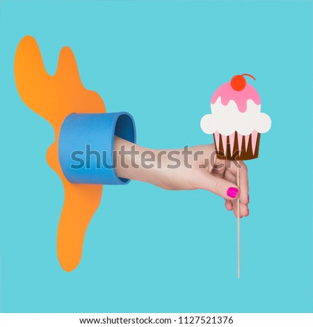 Woman`s hand with  colorful manicure holding a cake sticker in a paper craft composition. Isolated on a blue background. Art concept for beauty salon.