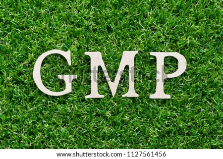Wood alphabet in word GMP (abbreviation of Good manufacturing pracice)on artificial green grass background