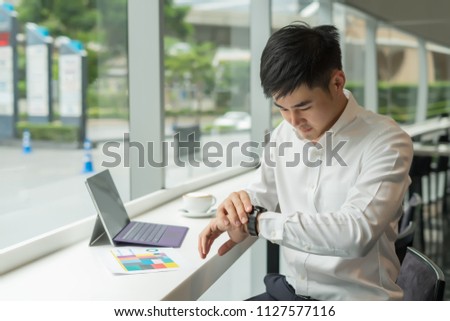 Handsome Asia businessman using laptop to analysis graph visualization and looking his watch  at coffee shop