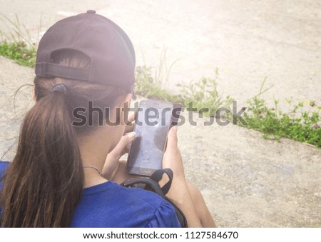 The girl in a baseball cap with the smartphone in hands.View from a back