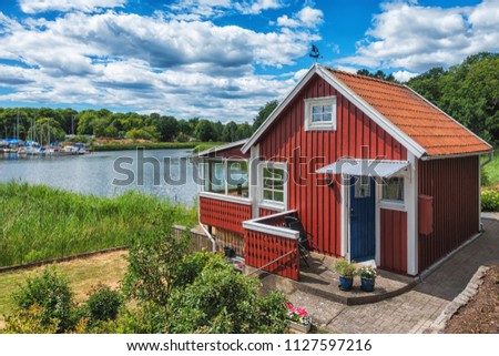 Red scandinavian wooden house on the lake with beautiful blue sky. Royalty-Free Stock Photo #1127597216