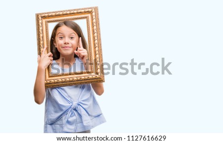 Brunette hispanic girl holding vintage art frame surprised with an idea or question pointing finger with happy face, number one