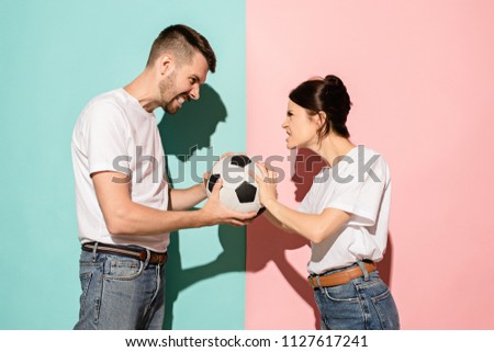 Fans of different teams. The unhappy and angry fans with ball on colored blue and pink background. The young man and woman are enemies. Fan, support concept. Human emotions concept.