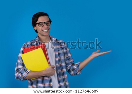 Smiley student holding two books pointing with one hand inviting or showing something on blue background.