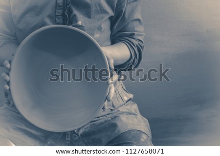 Photo in old vintage style. Master Potter holds round clay plate in his hands.Potter's body. Sculptor sculpts pots products from white clay. Workshop pottery. Master crock. Creativity.