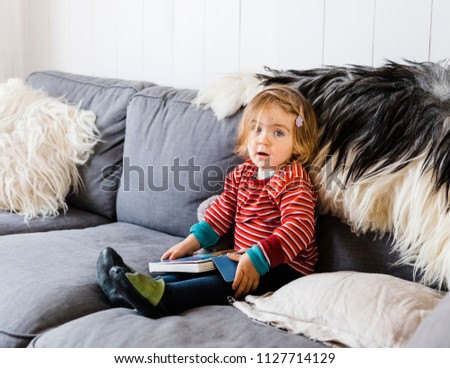 Toddler girl sitting on sofa with picture book - Hindeloopen, Netherlands